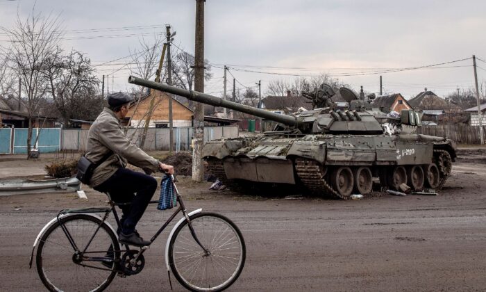 A man rides his bike past a destroyed Russian tank in Trostyanets, Ukraine, on March 30, 2022. (Chris McGrath/Getty Images)