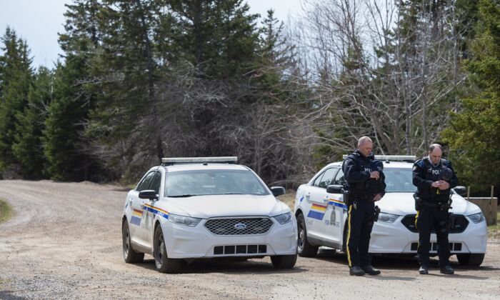 Two RCMP officers observe a moment of silence to honour slain Const. Heidi Stevenson and the other 21 victims of the mass killings at a checkpoint on Portapique Road in Portapique, N.S. on April 24, 2020. (The Canadian Press/Andrew Vaughan)