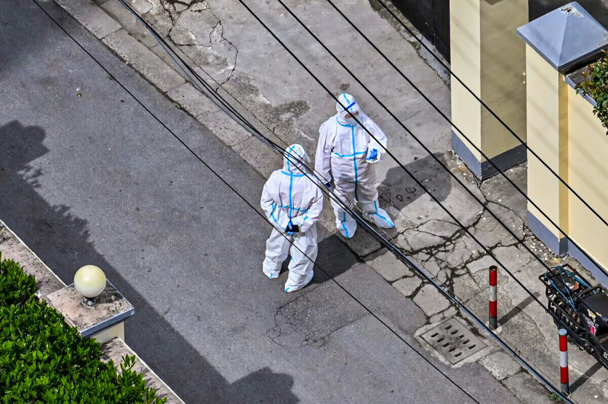 Workers wearing personal protective gear stand next to a residential compound during the second stage of a Covid-19 lockdown in Jing'an district in Shanghai on April 1, 2022. (Hector Retamal/AFP via Getty Images)