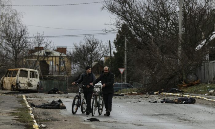Two person push their bicycle as they cross a street in Bucha, northwest of Kyiv, Ukraine, on April 2, 2022. (Ronaldo Schemidt/AFP via Getty Images)