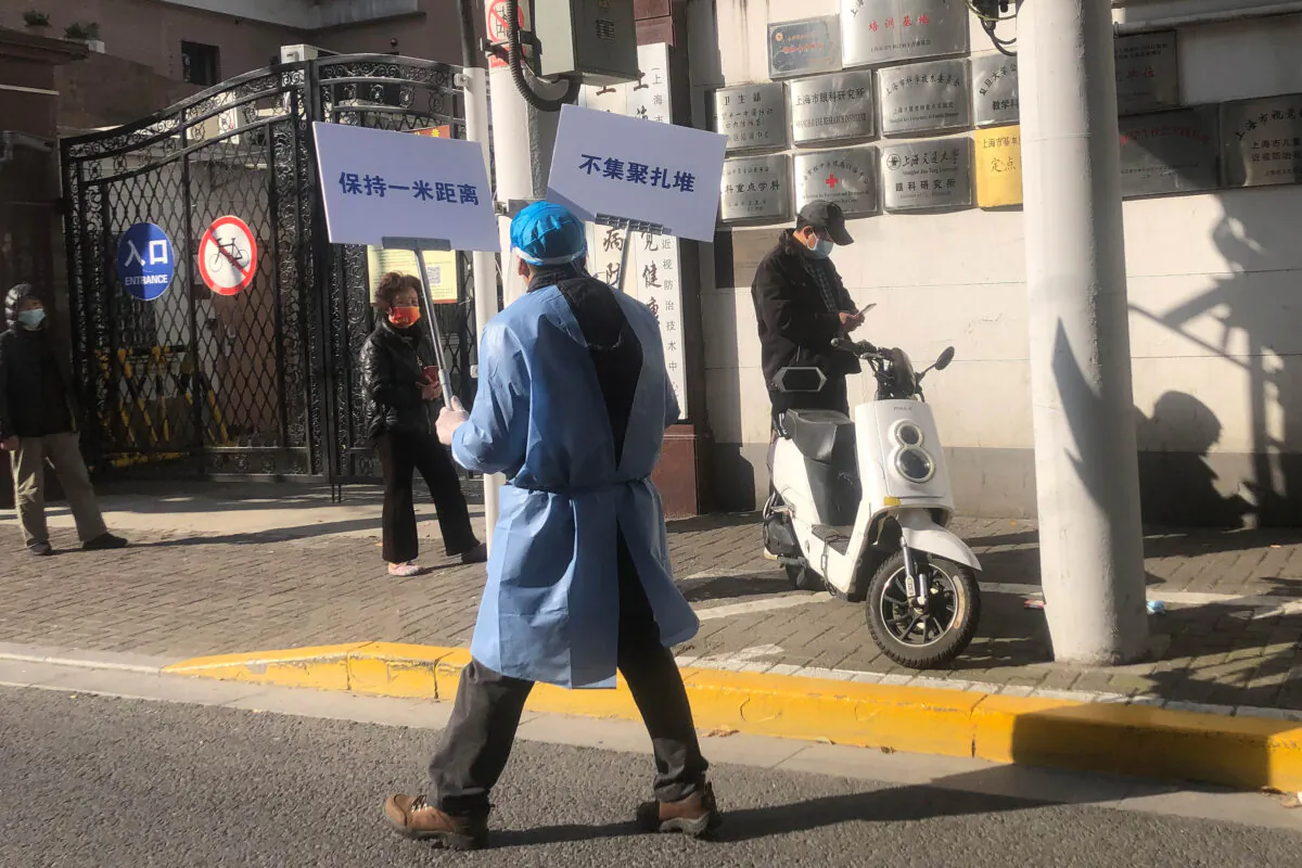 A worker holds up signs that say "Keep one meter distance" and "Do not crowd" as residents line up for mass COVID testing in a lockdown area in the Jingan district of western Shanghai, April 4, 2022. China has sent more than 10,000 health care workers from across the country to Shanghai, including 2,000 military medical staff, as China's largest city struggles to stamp out a rapidly spreading COVID-19 outbreak. (AP Photo/Chen Si)