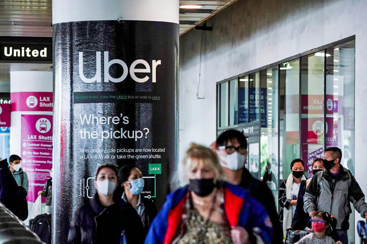 An Uber advertisement is seen behind travelers exiting the baggage claim area at the United Airlines terminal at Los Angeles International Airport (LAX), on Dec. 22, 2021. (Bing Guan/Reuters)
