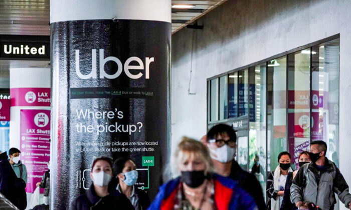An Uber advertisement is seen behind travelers exiting the baggage claim area at the United Airlines terminal at Los Angeles International Airport (LAX), on Dec. 22, 2021. (Bing Guan/Reuters)