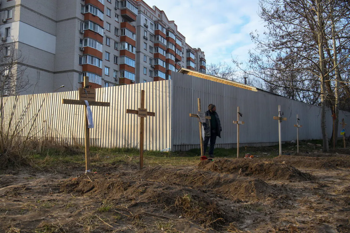 A man stands next to graves with bodies of civilians, who according to local residents were killed by Russian soldiers, in Bucha, near Kyiv, Ukraine, on April 4, 2022.  (Vladyslav Musiienko/Reuters)