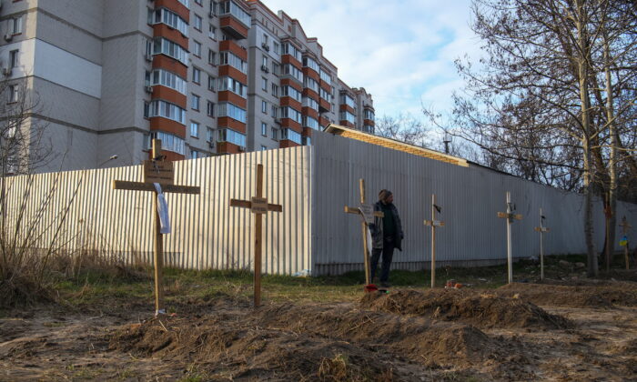 2022 年 4 月 4 日，在乌克兰基辅附近的布哈，一名男子站在坟墓旁，那里有平民尸体，据当地居民称，这些平民被俄罗斯士兵杀害。（Vladyslav Musiienko/路透社）