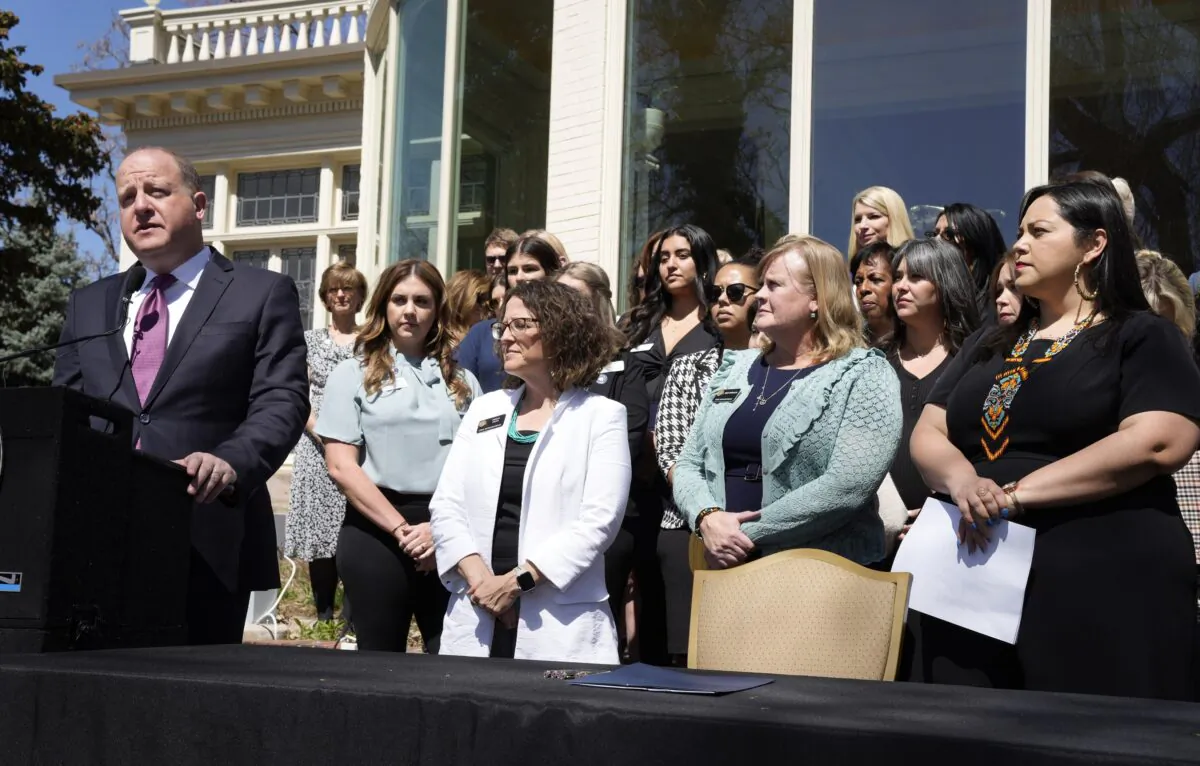 Colorado Governor Jared Polis speaks before signing a bill. Sen. Julie Gonzalez (R), Rep. Meg Froelich (C), and House majority leader Daneya Esgar (L), look on with guests and other lawmakers at the signing. (David Zalubowski/AP Photo)