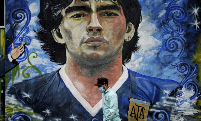 2021 年 11 月 25 日，在阿根廷布宜诺斯艾利斯的拉博卡，一位行人走过一幅描绘已故足球传奇人物迭戈·阿曼多·马拉多纳的壁画。（Mariana Nedelcu/路透社）
