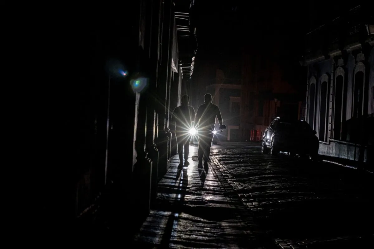 A cars headlights are seen past people walking on a dark in San Juan, Puerto Rico after a major power outage hit the island on April 6, 2022. (Ricardo Arduengo/AFP via Getty Images)
