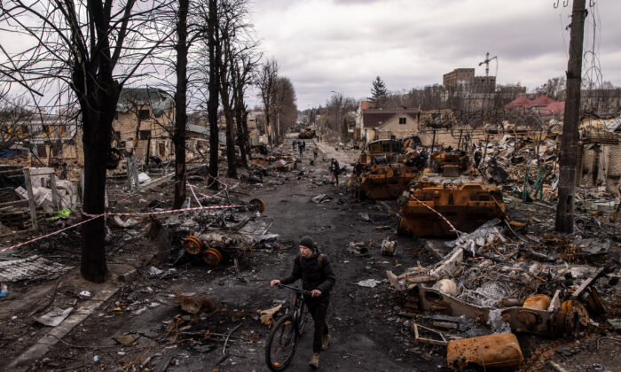 A man pushes his bike through debris and destroyed Russian military vehicles on a street in Bucha, Ukraine, on April 6, 2022. (TNS)