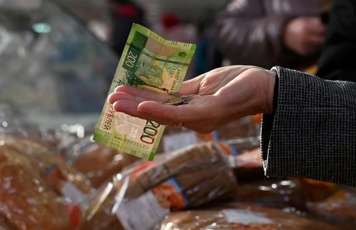 A customer hands over Russian ruble banknotes and coins to a vendor at a market in Omsk, Russia, on Oct. 29, 2021. (Reuters)