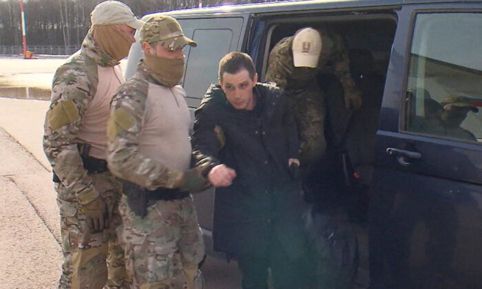 Former U.S. Marine Trevor Reed, who was detained in 2019 and accused of assaulting police officers, is escorted to a plane in Moscow, Russia, by Russian service members as part of a prisoner swap between the U.S. and Russia, in this still image taken from video released April 27, 2022. (RU24/Handout via REUTERS TV)