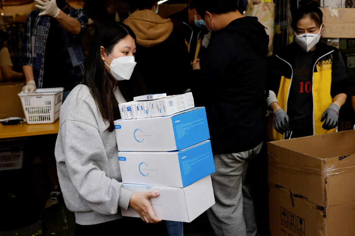 A woman wearing a protective mask buys boxes of Rapid antigen test kits for COVID-19 in Hong Kong, on Feb. 28, 2022. (Tyrone Siu/Reuters)