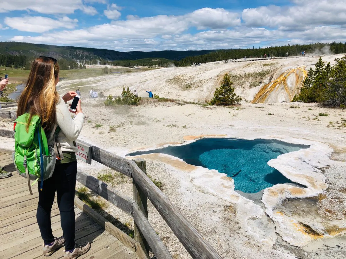 A woman takes photos of Blue Star spring near Old Faithful Upper Geyser Basin in Yellowstone National Park in Wyoming on June 11, 2019. National Park entrance fees are being waived on April 16, 2022. (Daniel Slim/AFP/Getty Images/TNS)