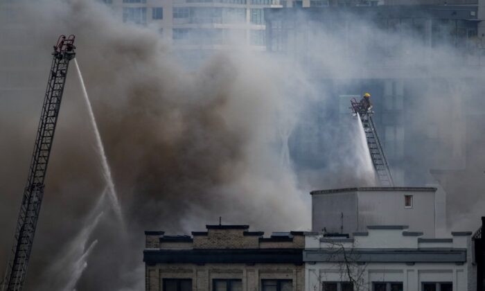 A firefighter on a ladder truck directs water on a four-alarm fire burning at a single room occupancy hotel in Vancouver, April 11, 2022. (The Canadian Press/Darryl Dyck)