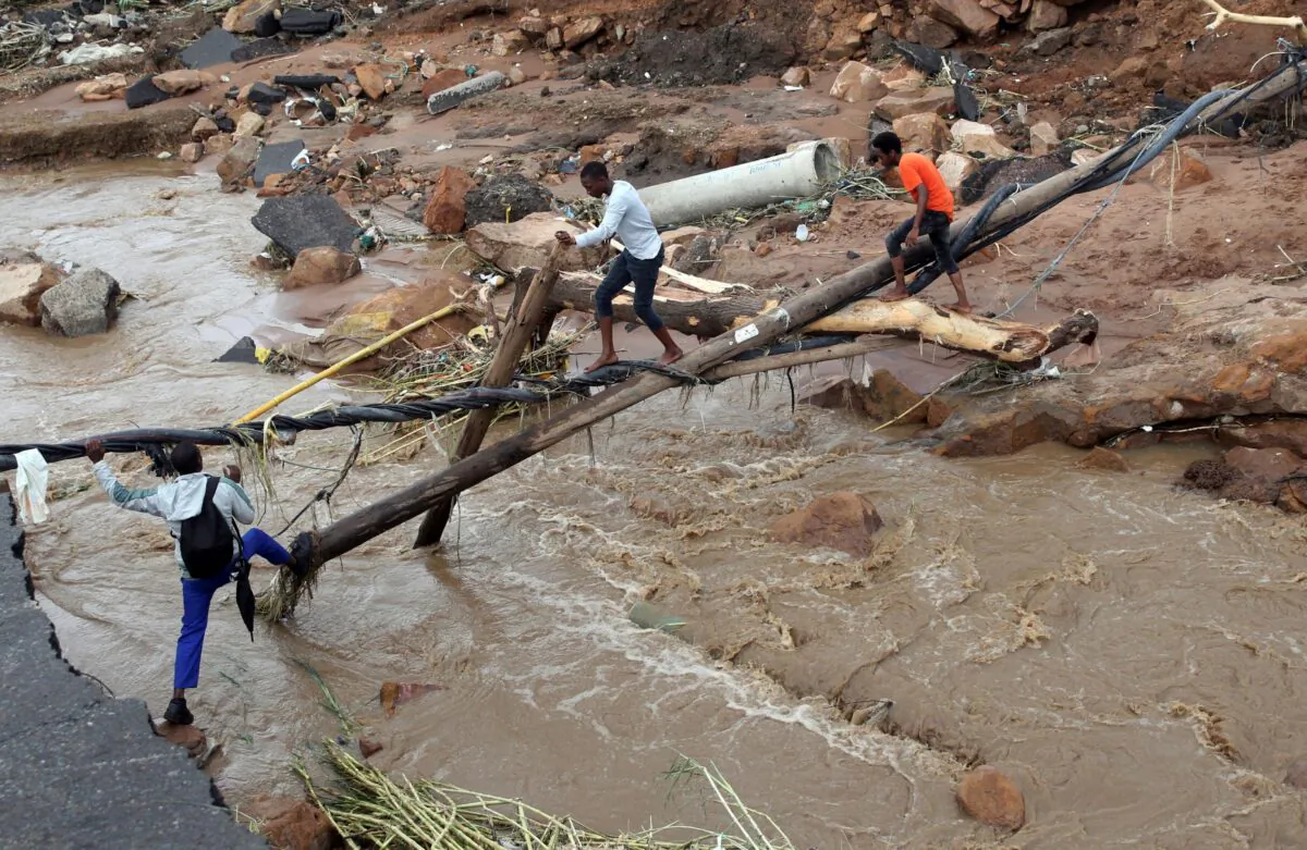 People walk across a makeshift bridge over a river, after a bridge was swept away in Ntuzuma, outside Durban, South Africa, on April 12, 2022. (Str/AP Photo)