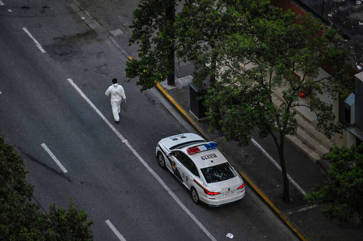A worker, wearing personal protective equipment (PPE), walks next to a police car on a street during a COVID-19 lockdown in the Jing'an district in Shanghai on April 11, 2022. (HECTOR RETAMAL/AFP via Getty Images)