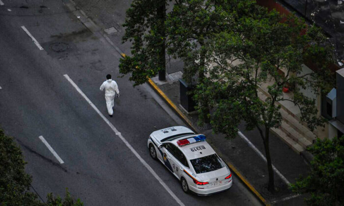 A worker, wearing personal protective equipment (PPE), walks next to a police car on a street during a COVID-19 lockdown in the Jing'an district in Shanghai on April 11, 2022. (HECTOR RETAMAL/AFP via Getty Images)