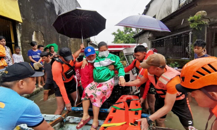 Rescue personnel assist a woman onto a raft amidst flooding, after the tropical storm Megi hit, in Leyte Province, Philippines April 10, 2022. Picture taken April 10, 2022. (Philippine Coast Guard/Handout via Reuters)
