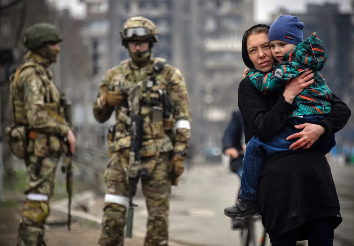 A woman holds a child next to Russian soldiers in a street of Mariupol, on April 12, 2022.  (Alexander Nemenov/AFP via Getty Images)