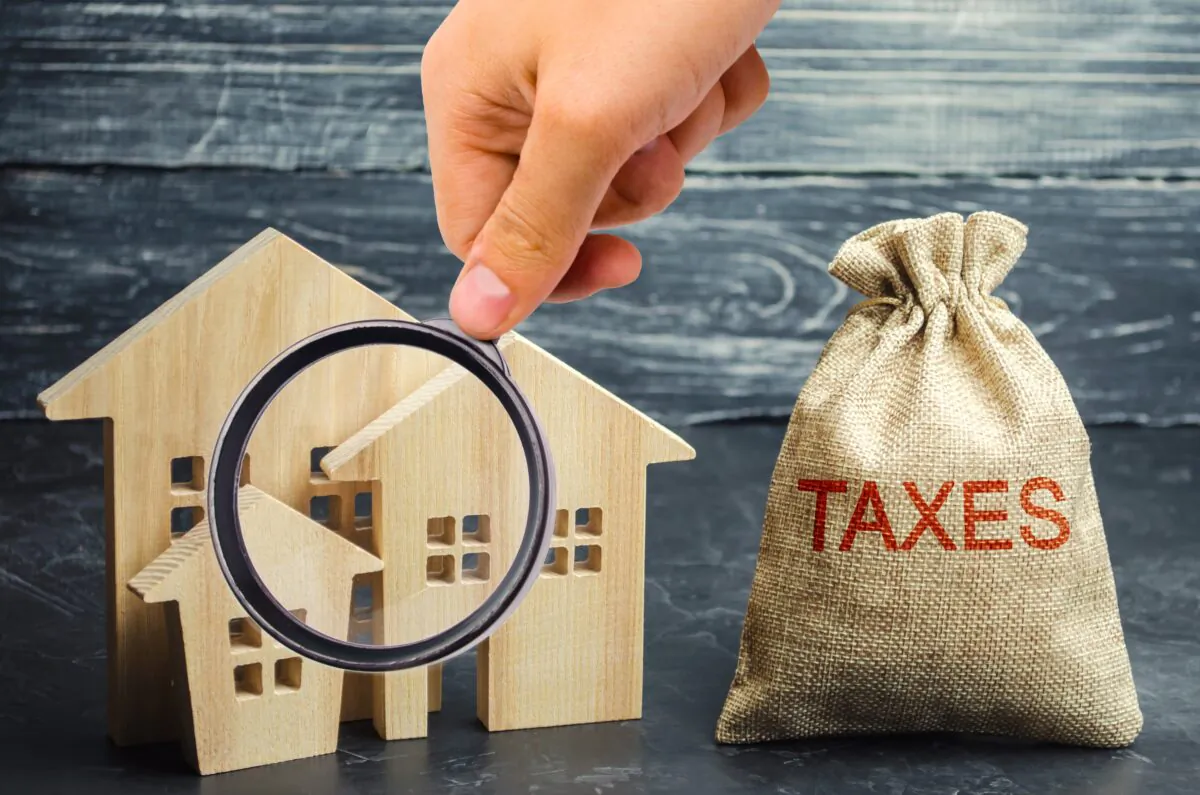 Bag with the money and the word Taxes and wooden houses. Owning a house means you need to pay property tax. (Andrii Yalanskyi/Shutterstock)