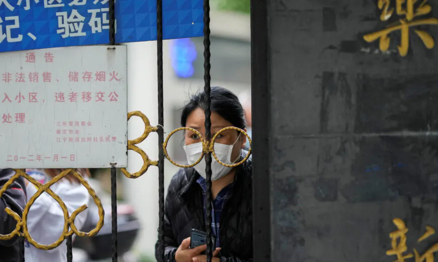 A resident looks out behind a gate blocking an entrance to a residential area under COVID lockdown in Shanghai on April 13, 2022. (Aly Song/Reuters)