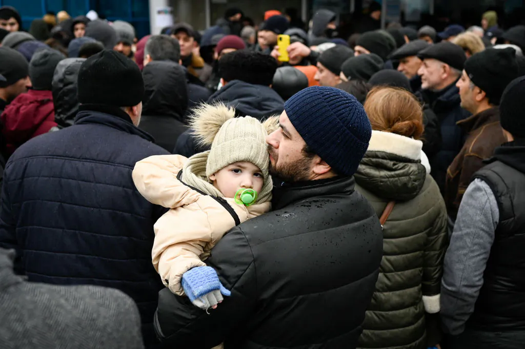 A man holds his child as families, who fled Ukraine due to the Russian invasion, wait to enter a refugee camp in the Moldovan capital Chisinau, on March 3, 2022. (Nikolay Doychinov/AFP via Getty Images)