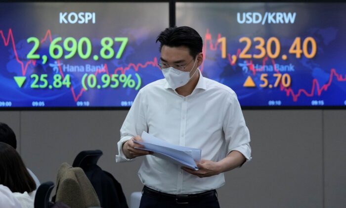 A currency trader passes by screens showing the Korea Composite Stock Price Index (KOSPI) (L) and the foreign exchange rate between U.S. dollar and South Korean won, at the foreign exchange dealing room of the KEB Hana Bank headquarters in Seoul, South Korea, on April 15, 2022. (Ahn Young-joon/AP Photo)
