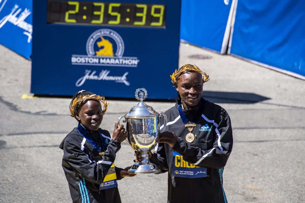 Peres Jepchirchir (L) and Evans Chebet hold the victory trophy over the finish line after both took first place in their divisions in the 126th Boston Marathon in Boston on April 18, 2022. (Joseph Prezioso/AFP via Getty Images)