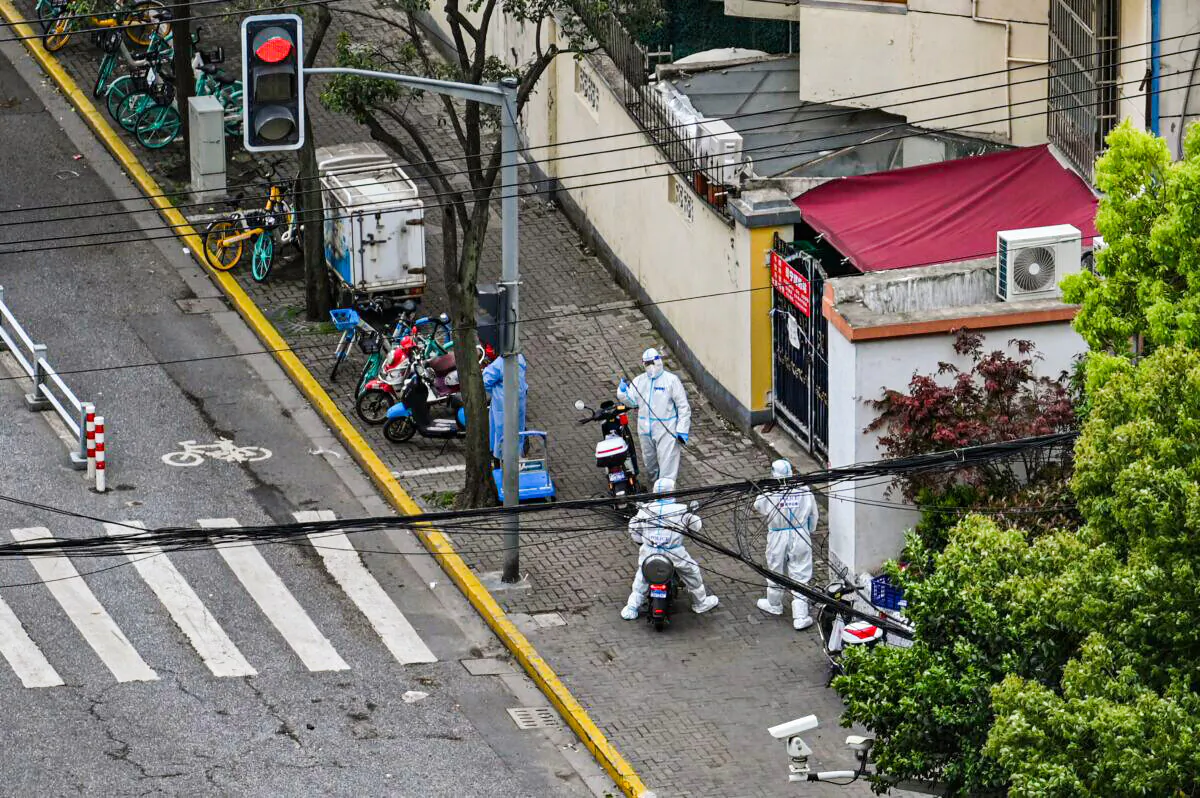 Policemen wearing personal protective equipment (PPE) stand next to the entrance of a neighborhood during a COVID-19 coronavirus lockdown in the Jing'an district in Shanghai on April 15, 2022. (HECTOR RETAMAL/AFP via Getty Images)