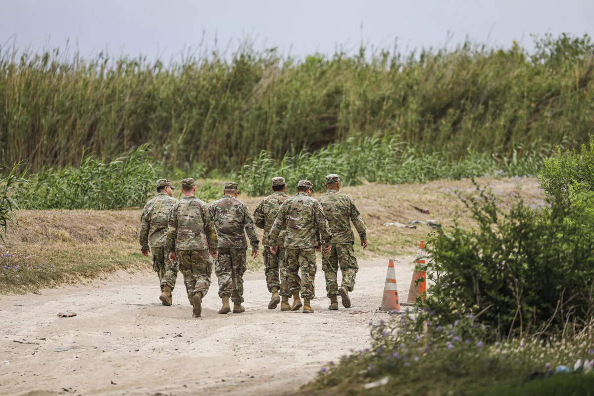 A group of Texas National Guardsmen walk toward a group of Cubans who just crossed the Rio Grande illegally from Mexico into Eagle Pass, Texas, on April 19, 2022. (Charlotte Cuthbertson/The Epoch Times)