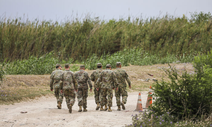 A group of Texas National Guardsmen walk toward a group of Cubans who just crossed the Rio Grande illegally from Mexico into Eagle Pass, Texas, on April 19, 2022. (Charlotte Cuthbertson/The Epoch Times)