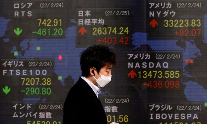 A man wearing a protective mask walks past an electronic board displaying Russian Trading System (RTS) Index, Japan's Nikkei index, and the Dow Jones Industrial Average outside a brokerage in Tokyo, Japan, on Feb. 25, 2022. (Kim Kyung-Hoon/Reuters)