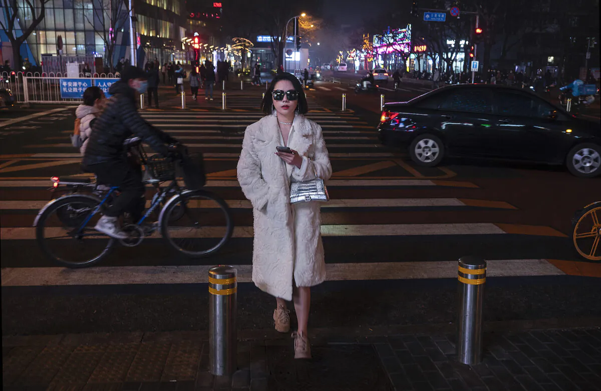 A woman walks across a road at a traffic light in a high-end shopping district on a polluted and foggy evening in Beijing, China on March 24, 2022. (Kevin Frayer/Getty Images)