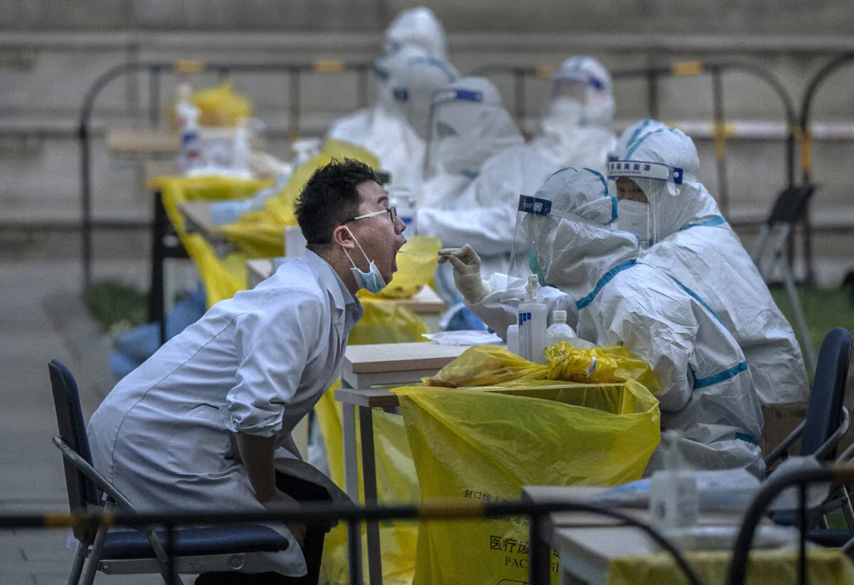 A health worker wears a protective suit as he swabs an employee from a local company  to get a sample for nucleic acid testing for the COVID-19 virus at a makeshift testing site in Haidian District on April 26, 2022 in Beijing, China (Kevin Frayer/Getty Images)