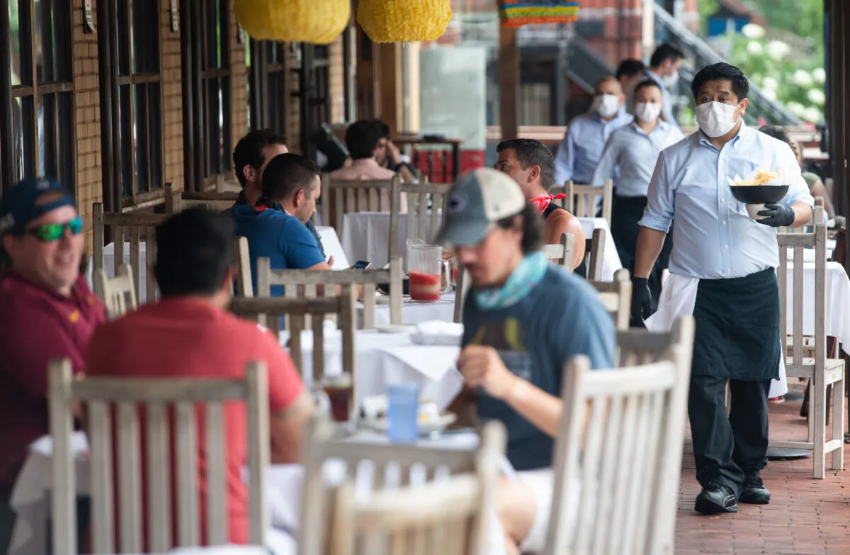 A waiter wearing a mask and gloves delivers food to a table to customers seated at an outdoor patio at a Mexican restaurant in Washington, on May 29, 2020. (Saul Loeb/AFP via Getty Images)