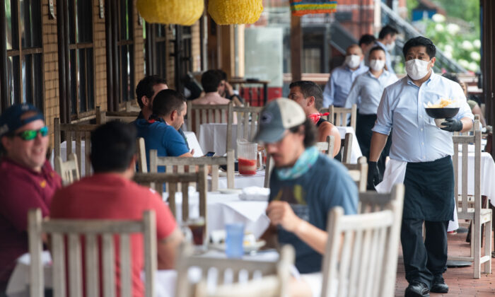 A waiter wearing a mask and gloves delivers food to a table to customers seated at an outdoor patio at a Mexican restaurant in Washington, on May 29, 2020. (Saul Loeb/AFP via Getty Images)