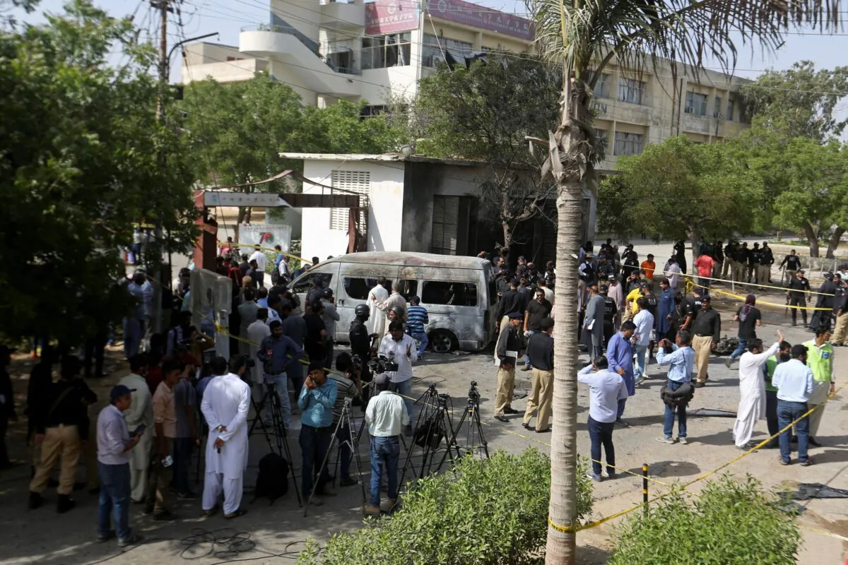 Pakistani police officers and journalists gather near a burned van at the site of an explosion, in Karachi, Pakistan, on April 26, 2022. (Fareed Khan/AP Photo)