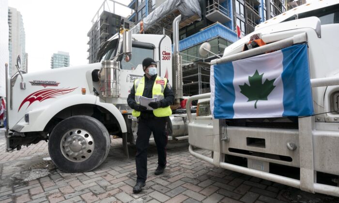 A police officer walks between parked trucks as he distributes a notice to protesters, Feb. 16, 2022 in Ottawa.(The Canadian Press/Adrian Wyld)