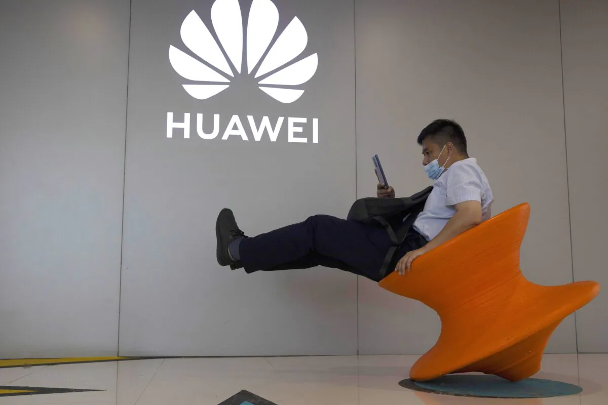 A man wearing a mask sits near a Huawei store logo in Beijing, China, on July 31, 2020. (Ng Han Guan/AP Photo)