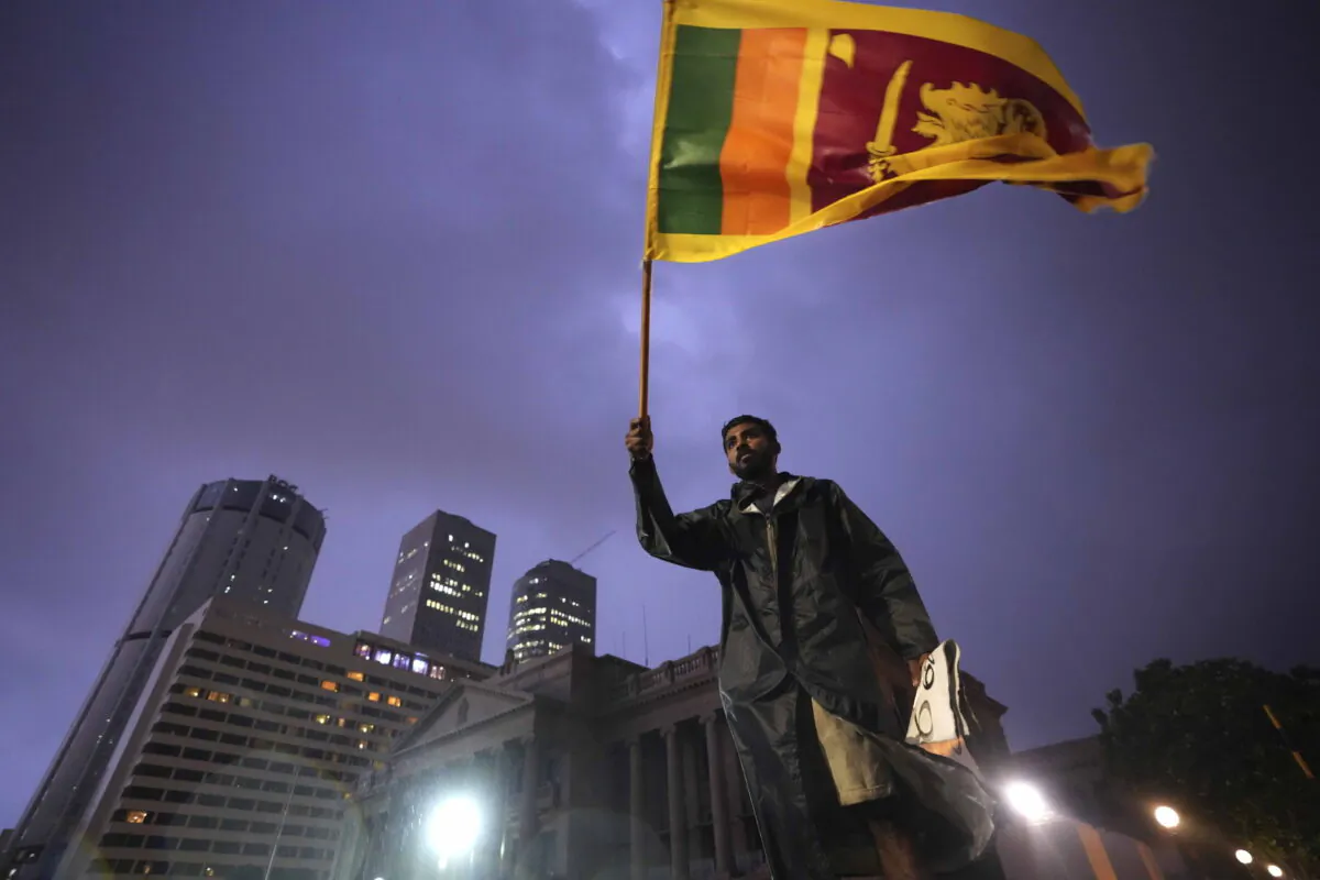 A man waves a Sri Lankan national flag as he stands on a barricade blocking the entrance to president's office during a protest in Colombo, Sri Lanka, on April 11, 2022. Thousands of Sri Lankans protested calling on the country's president Gotabaya Rajapaksa to resign amid worst economic crisis in history. (Eranga Jayawardena/AP Photo)