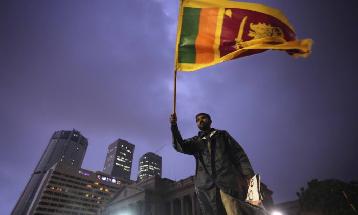 A man waves a Sri Lankan national flag as he stands on a barricade blocking the entrance to president's office during a protest in Colombo, Sri Lanka, on April 11, 2022. (Eranga Jayawardena/AP Photo)