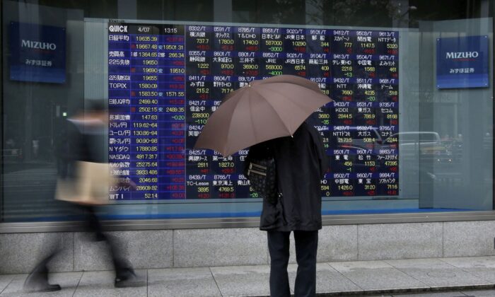 A man holding an umbrella looks at an electronic stock quotation board outside a brokerage in Tokyo, on April 7, 2015. (Issei Kato/Reuters)
