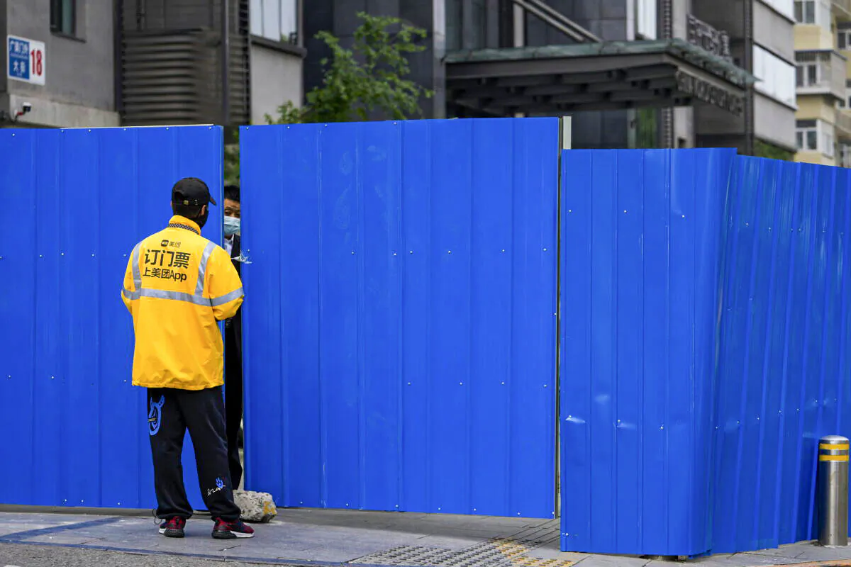 A delivery worker chats with a masked security guard at a barricaded fence of a locked-down residential complex in Beijing on April 29, 2022. (Andy Wong/AP Photo)