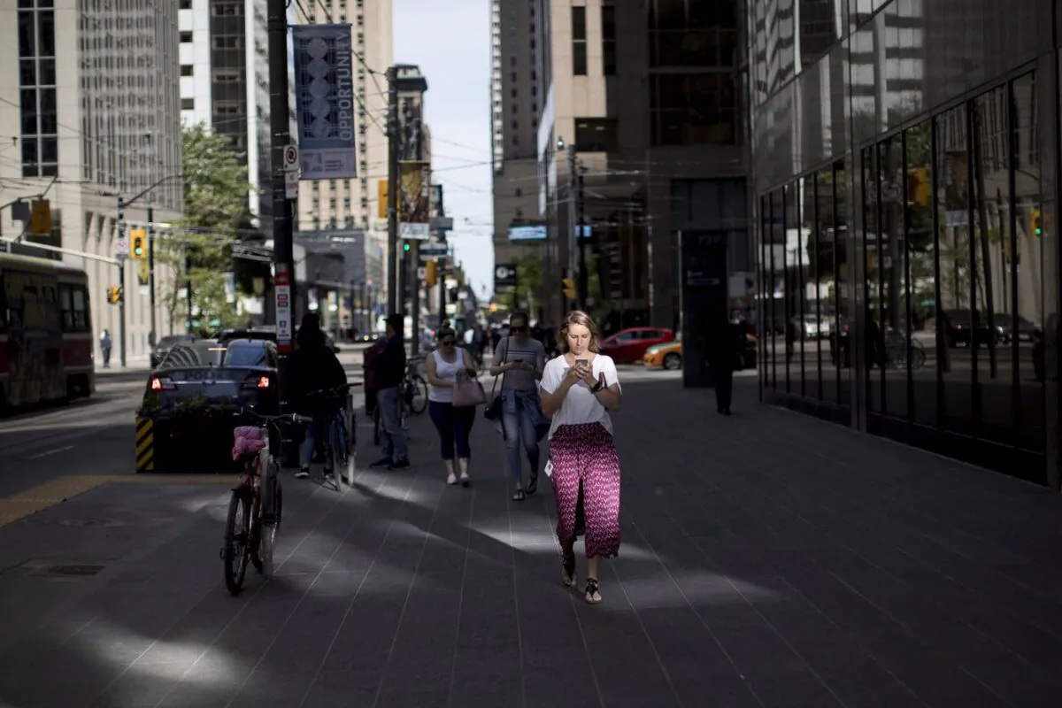 A woman looks down at her cell phone while walking though downtown Toronto, on June 12, 2018. (The Canadian Press/Chris Young)