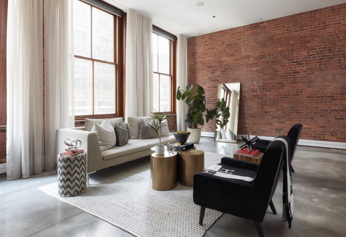 A living room with an exposed brick wall is paired with black and brass accents. (Scott Gabriel Morris/TNS)