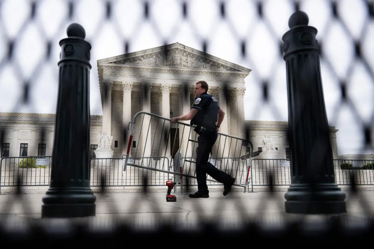 A police officer carrying a barricade is seen through un-scalable fence that stands around the U.S. Supreme Court on May 5, 2022. (JIM WATSON/AFP via Getty Images)