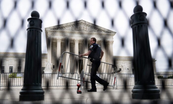 A police officer carrying a barricade is seen through un-scalable fence that stands around the U.S. Supreme Court on May 5, 2022. (JIM WATSON/AFP via Getty Images)