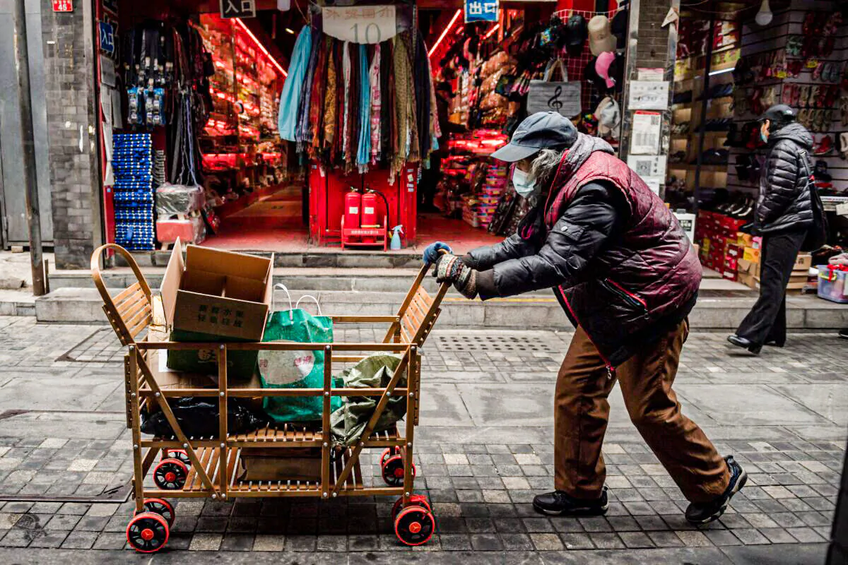 An elderly woman pushes a cart after searching through garbage bins to collect recyclable items to sell, along a street near the Great Hall of the People in Beijing, on March 5, 2021. (Nicolas Asfouri/AFP via Getty Images)