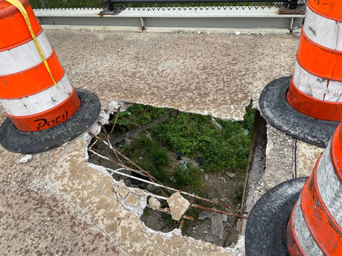 The ground below an elevated pedestrian bridge spanning the M-10 Lodge freeway in Detroit is visible through a hole in the concrete, large enough for a person to fall through. Ely Hydes, walking the footbridge to a Detroit Tigers game said he fell 15 feet to the ground when part of the concrete collapsed on May 9, 2022. (Kevin Hardy/Detroit News via AP)