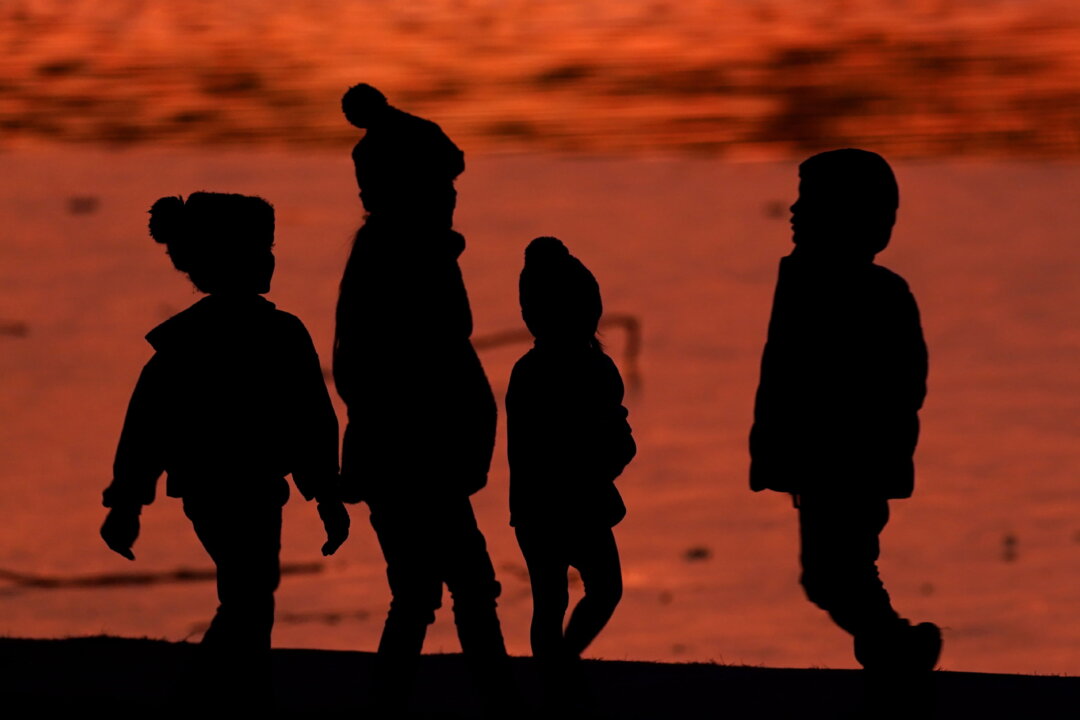 Children are silhouetted against a pond at a park in Lenexa, Kan., on Dec. 26, 2020. (Charlie Riedel/AP Photo)